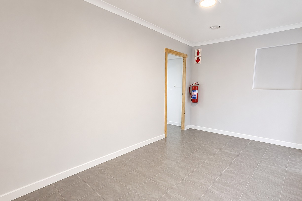 A clean, empty office space featuring neutral grey walls, tiled flooring, a recessed wall niche, and essential fire safety equipment.