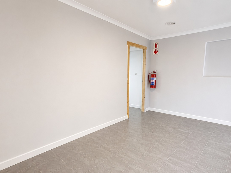 A clean, empty office space featuring neutral grey walls, tiled flooring, a recessed wall niche, and essential fire safety equipment.