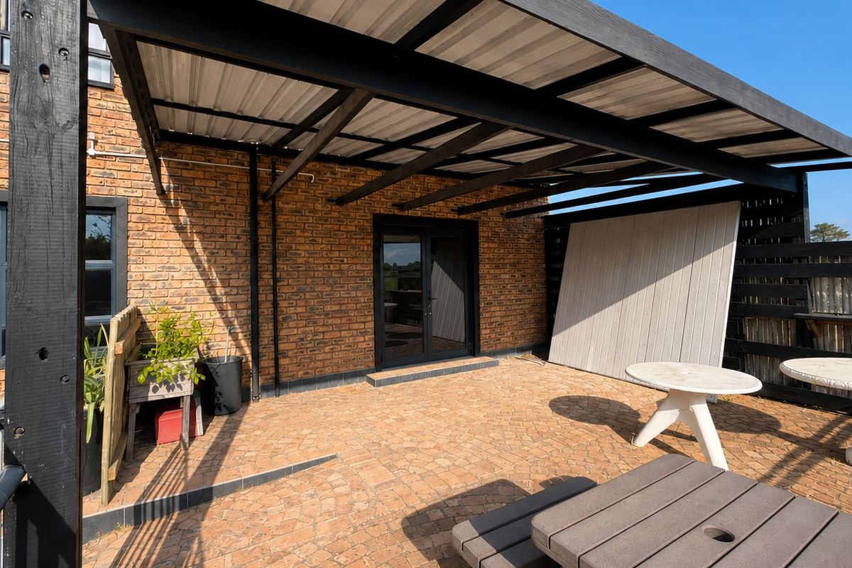 A covered outdoor patio area featuring a brick facade, timber pergola structure, and paved flooring, providing a functional space for outdoor office breaks.