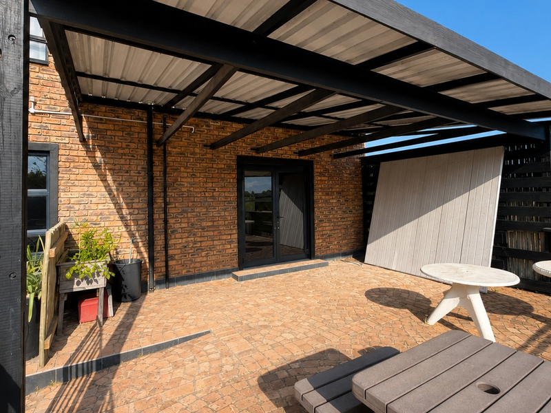 A covered outdoor patio area featuring a brick facade, timber pergola structure, and paved flooring, providing a functional space for outdoor office breaks.