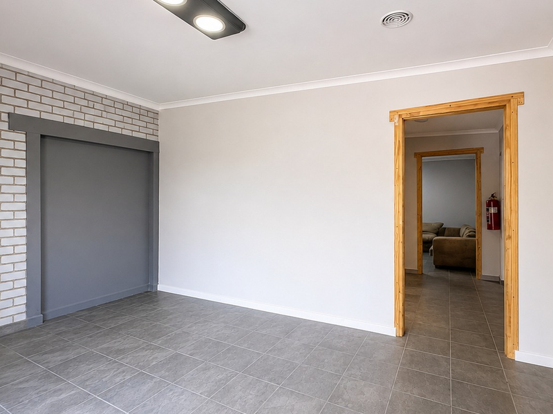 A bright, empty office space featuring tiled flooring, a grey brick feature wall, and a clean, neutral aesthetic with a connecting doorway.