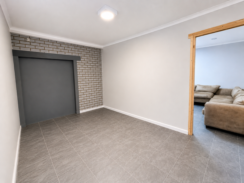 A bright, empty office space featuring modern grey tiled flooring, a decorative exposed brick wall, and clean neutral finishes.