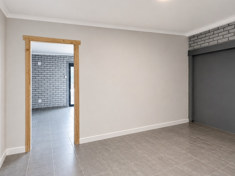 A bright, empty office space featuring neutral walls, tiled flooring, and a modern grey exposed brick feature wall.