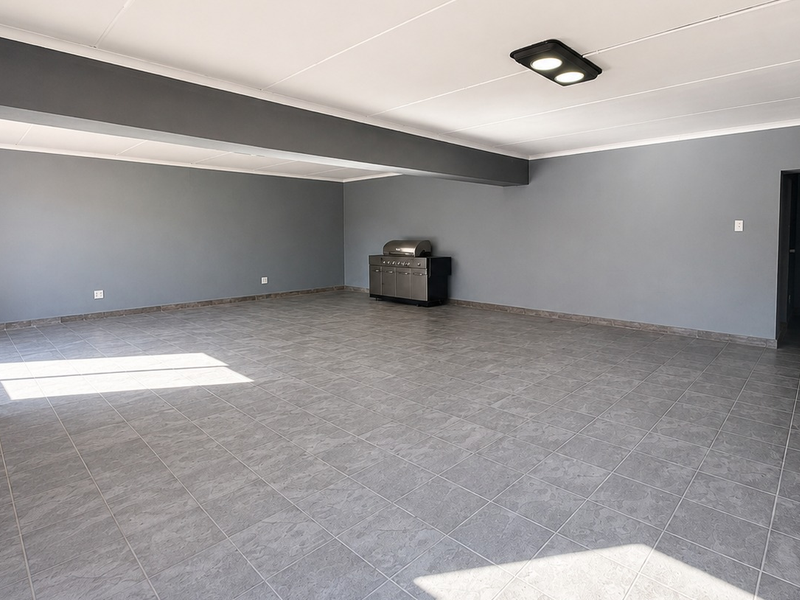 Spacious, open-plan office area featuring neutral grey walls, durable tiled flooring, an exposed brick feature pillar, and integrated ceiling lighting.