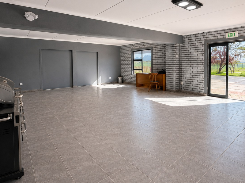 Spacious open-plan office area featuring tiled flooring, exposed brick accents, and direct access to an outdoor area through a sliding glass door.