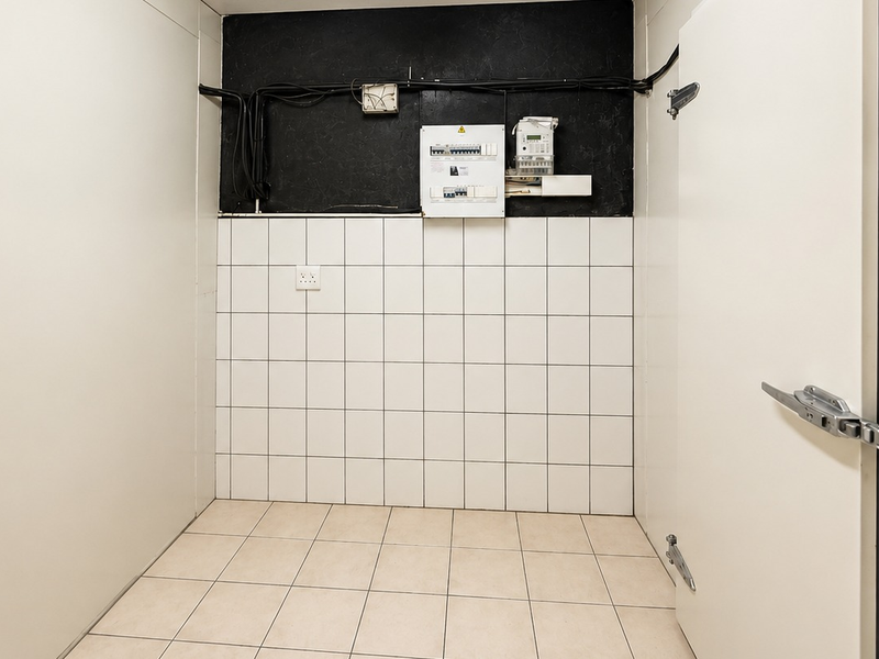 A clean utility or storage space featuring tiled surfaces, industrial-style doors, and a wall-mounted electrical distribution board.