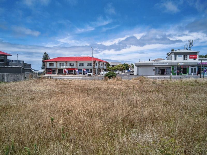 A vacant commercial plot of land situated in a developed area with surrounding commercial buildings and street access.