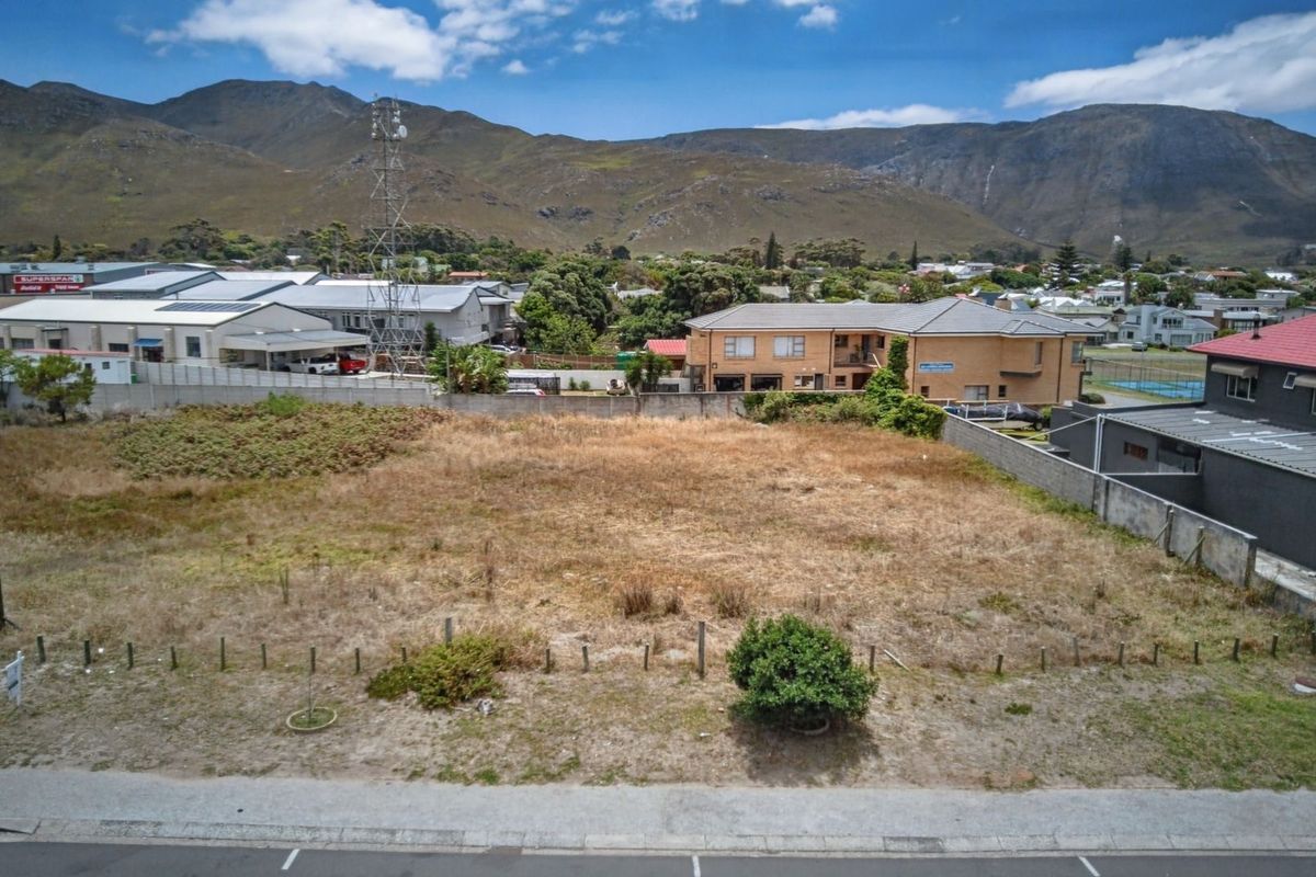 An aerial view of a vacant commercial land plot featuring boundary walls and street frontage, set against a mountain backdrop.