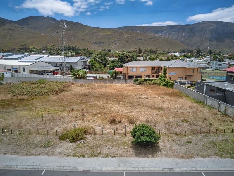 An aerial view of a vacant commercial land plot featuring boundary walls and street frontage, set against a mountain backdrop.