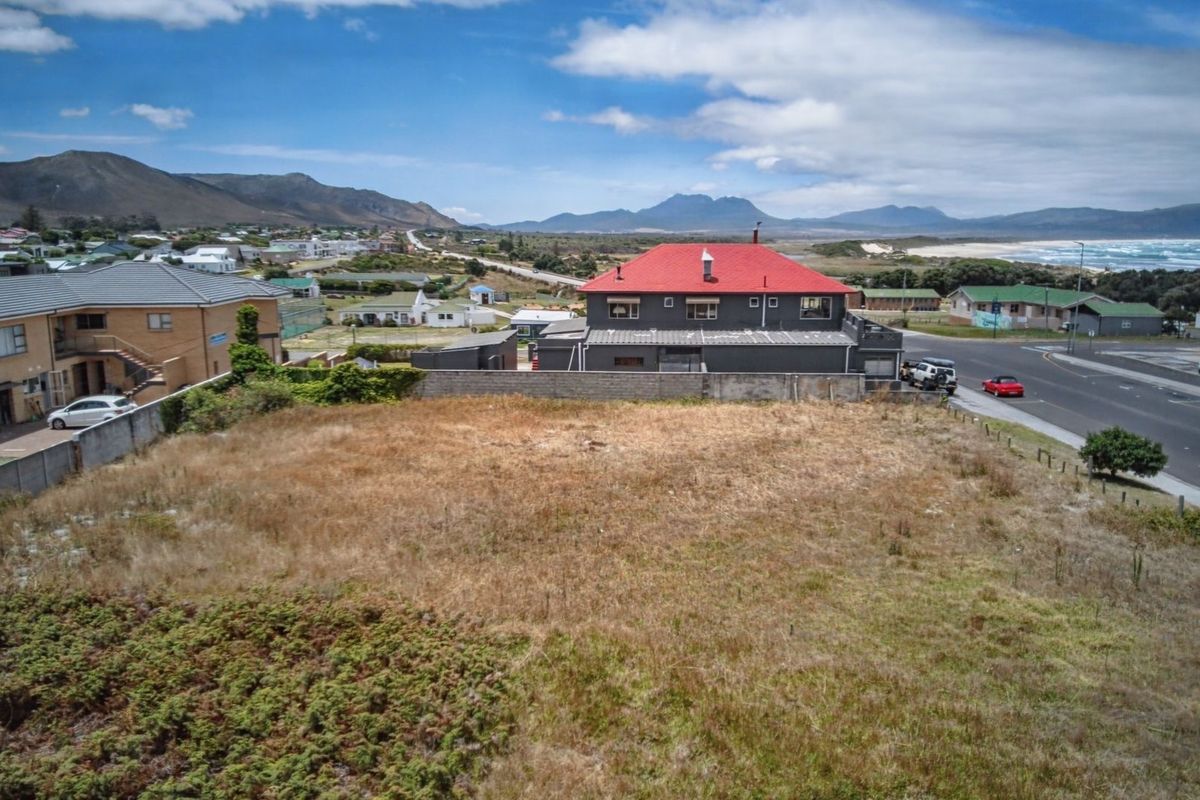 Aerial view of a vacant commercial plot featuring boundary walls and direct street access, situated in a coastal neighborhood with mountain and sea views.