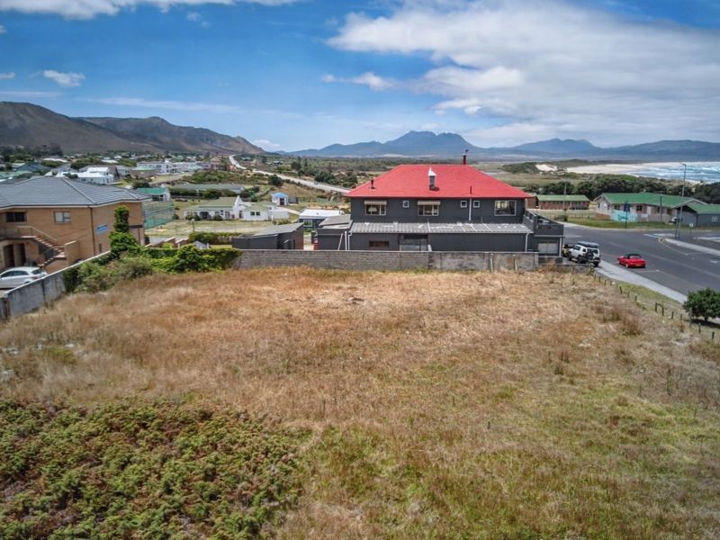 Aerial view of a vacant commercial plot featuring boundary walls and direct street access, situated in a coastal neighborhood with mountain and sea views.