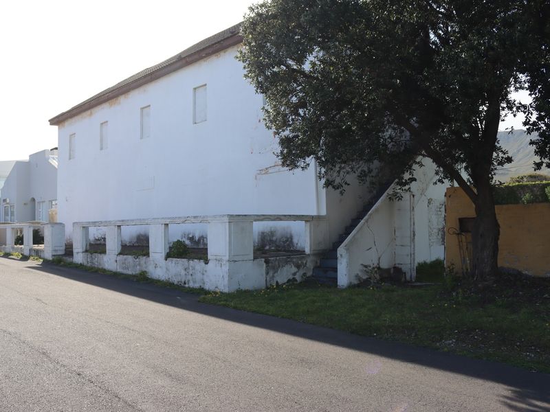Street-facing view of a commercial building featuring a white facade, external staircase, and concrete boundary wall showing signs of weathering.