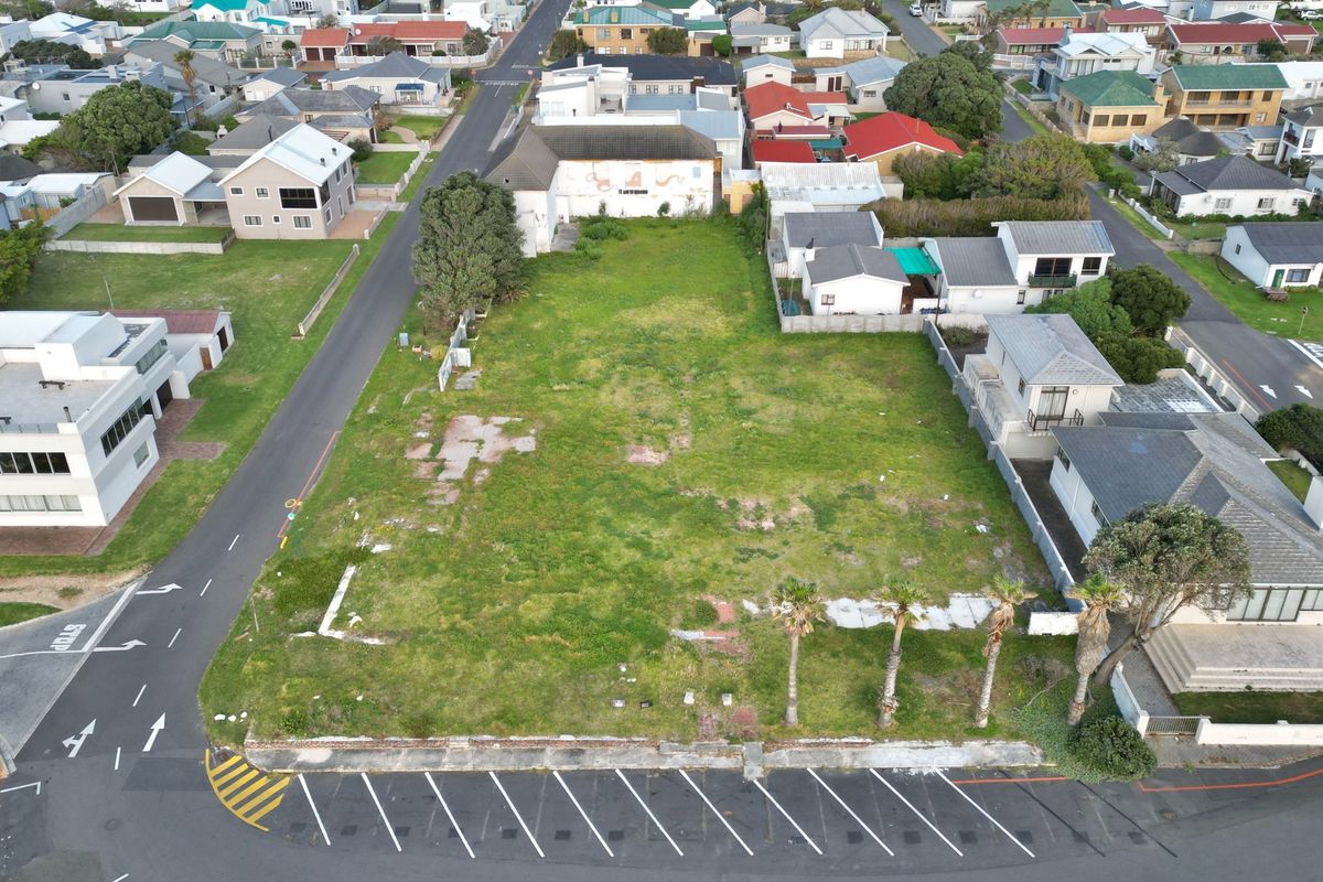Aerial view of a vacant commercial plot featuring a paved parking area, boundary walls, and established palm trees in a residential neighborhood.