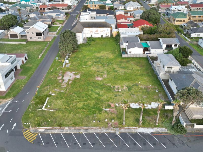 Aerial view of a vacant commercial plot featuring a paved parking area, boundary walls, and established palm trees in a residential neighborhood.