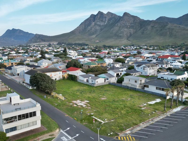 Aerial view of a vacant commercial plot situated in a developed residential area with mountain views and convenient road access.