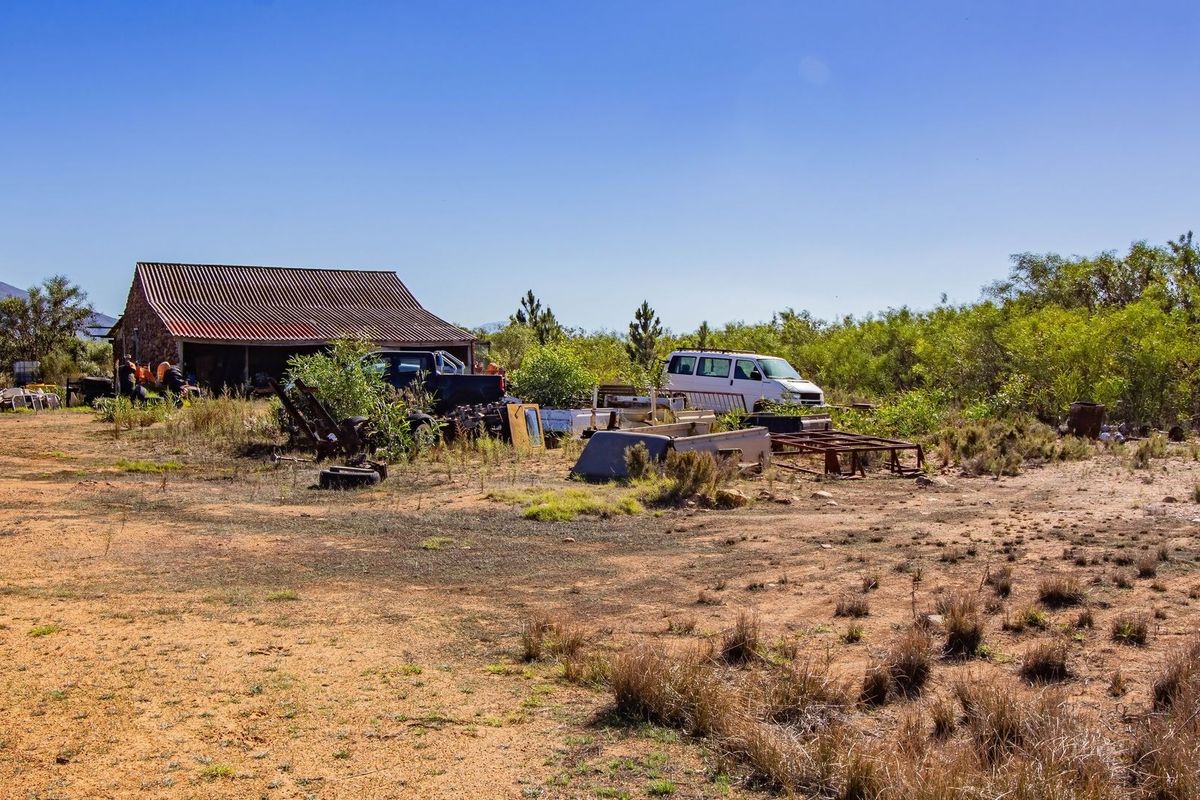 A view of a vacant commercial plot featuring a rustic stone structure with a corrugated metal roof, surrounded by open land and natural vegetation.