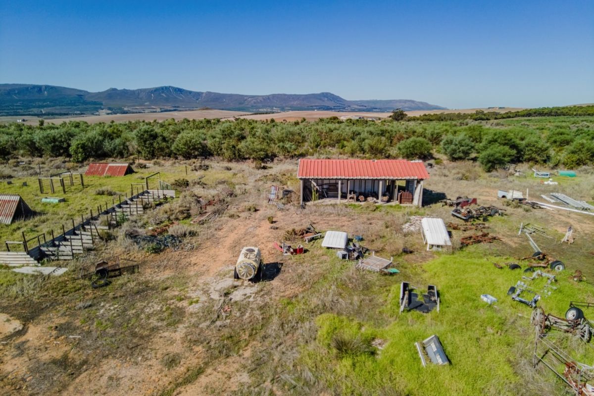 Aerial view of a vacant commercial plot featuring an open-sided shed with a red corrugated metal roof and surrounding rural landscape.
