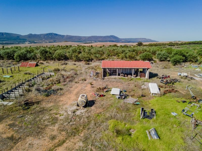 Aerial view of a vacant commercial plot featuring an open-sided shed with a red corrugated metal roof and surrounding rural landscape.