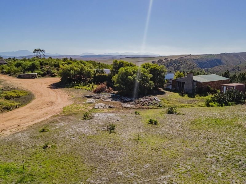 Aerial view of a vacant commercial land plot featuring a dirt access road, existing brick structure with stone chimney, and expansive rural landscape.