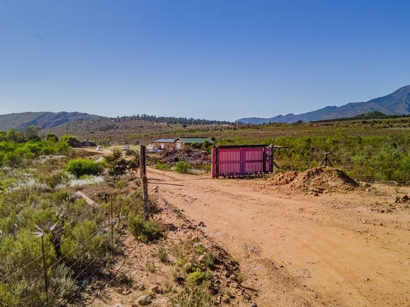 A view of the property entrance featuring a dirt access road, perimeter fencing, and a gate, set against a scenic mountain landscape.