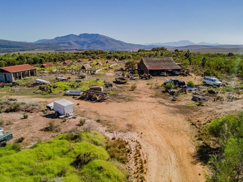 Aerial view of a large commercial vacant land plot featuring multiple outbuildings, dirt access roads, and expansive open terrain with mountain views.