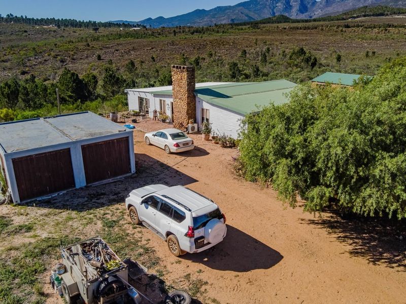 Aerial view of a rural commercial property featuring a main building with a stone chimney, a detached double garage, and surrounding natural landscape.