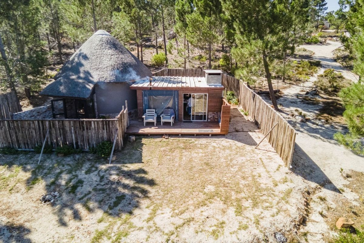 Aerial view of a rustic farm dwelling featuring a traditional thatched roof section, timber decking, and an outdoor fireplace within a fenced garden area.