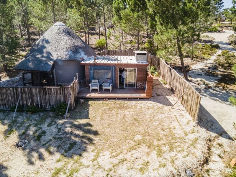 Aerial view of a rustic farm dwelling featuring a traditional thatched roof section, timber decking, and an outdoor fireplace within a fenced garden area.