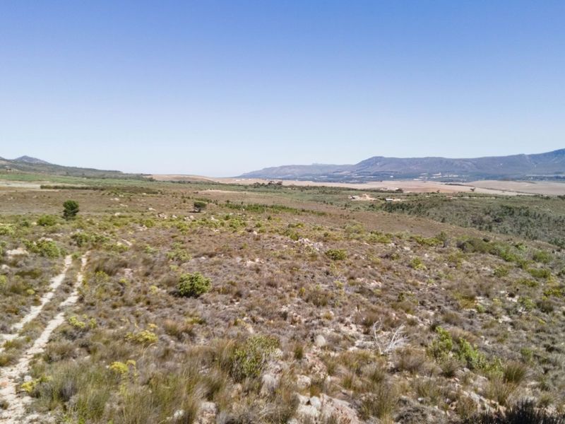 An expansive aerial view of the natural farm landscape featuring rolling hills and a dirt track path.