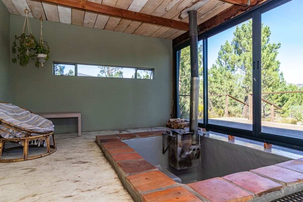 A unique living space featuring a sunken conversation pit with a built-in wood-burning stove, exposed timber ceiling, and large sliding doors opening to nature.