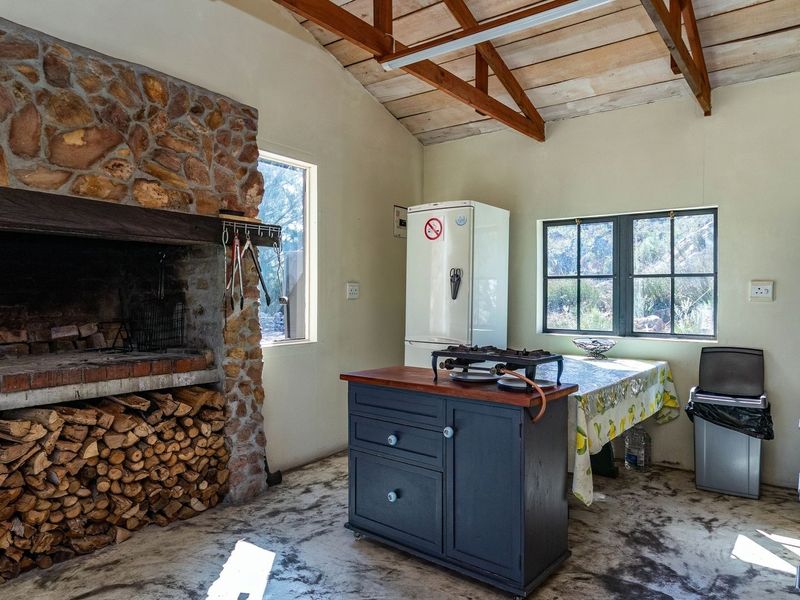 Rustic kitchen area featuring a large stone fireplace, exposed timber roof trusses, and concrete flooring, offering a traditional farm-style aesthetic.