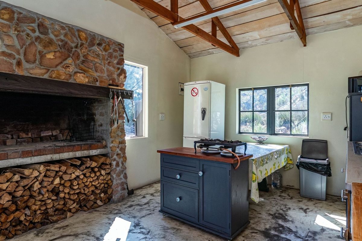 Rustic kitchen area featuring a large stone fireplace, exposed timber roof trusses, and concrete flooring, offering a traditional farm-style aesthetic.