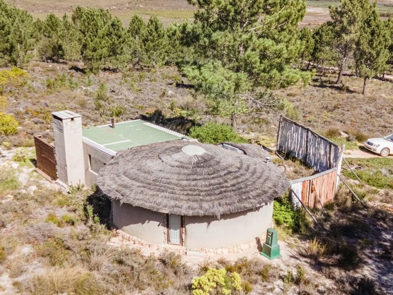 Aerial view of a rustic farm dwelling featuring a traditional thatched roof, masonry chimney, and surrounding natural landscape.