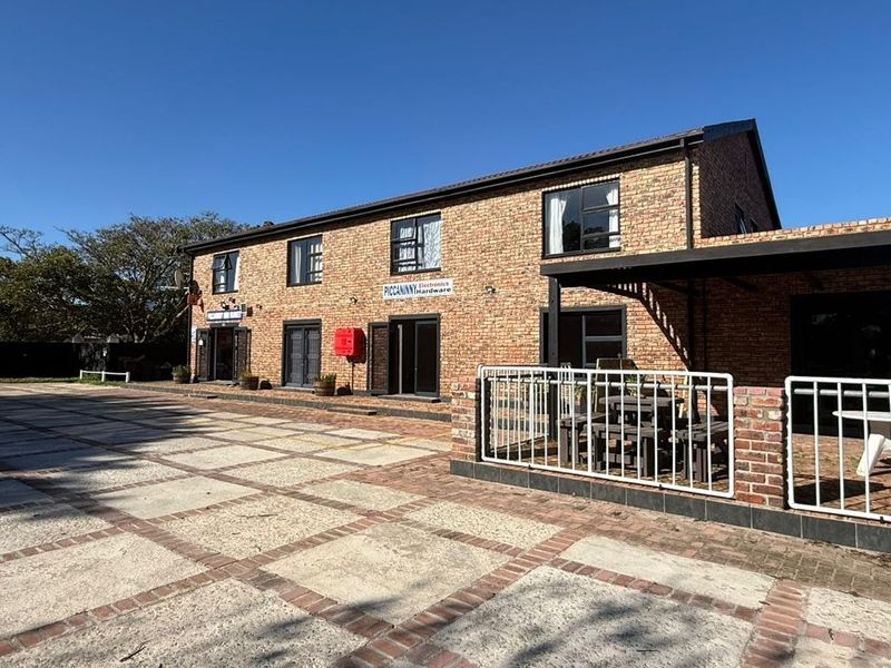 Commercial property featuring a face brick facade, paved driveway, and a covered patio area with metal railings.