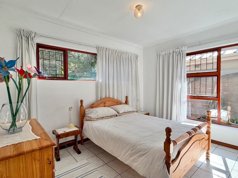 A bright bedroom featuring tiled flooring, timber-framed windows with security bars, and neutral wall finishes.