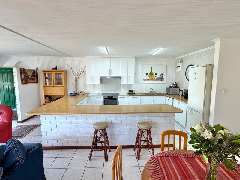 Open-plan kitchen featuring a U-shaped layout with a brick breakfast bar, white cabinetry, and tiled flooring, seamlessly connecting to the living and dining areas.