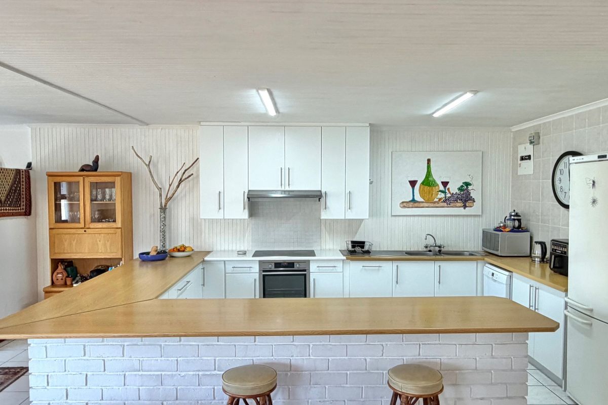A functional kitchen featuring white cabinetry, a breakfast bar with a brick base, integrated oven and hob, and tiled splashback finishes.
