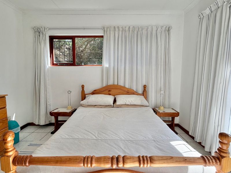 A functional bedroom featuring tiled flooring and wooden window frames with security bars, offering a simple and clean living space.