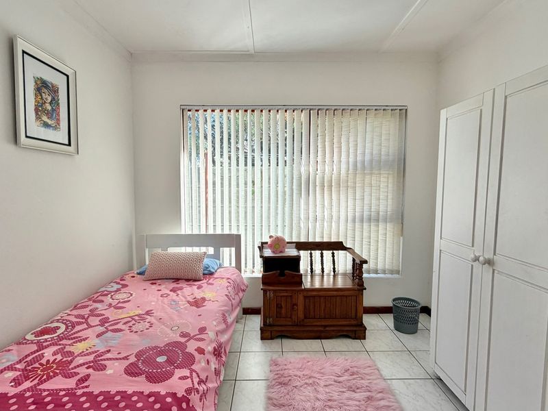 A functional bedroom featuring tiled flooring, a built-in wardrobe, and vertical blinds covering the window.