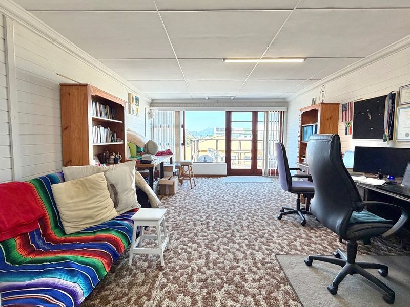 Spacious living area featuring timber-clad walls, patterned carpeting, and direct access to an outdoor balcony through sliding glass doors.