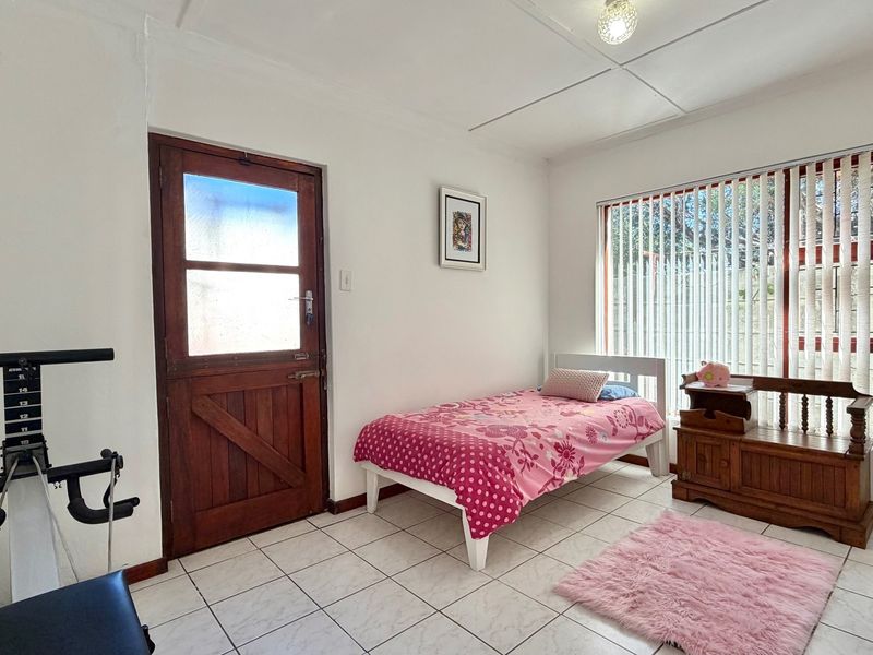 A functional bedroom featuring tiled flooring, vertical blinds, and a wooden exterior door, providing direct access to the outside area.
