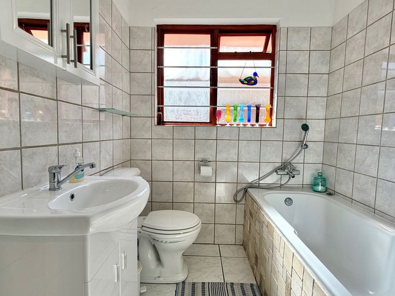 A functional bathroom featuring a vanity basin, toilet, and a bathtub with a handheld shower mixer, finished with neutral wall and floor tiling.