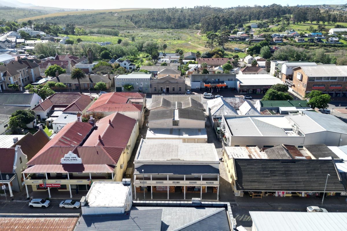 Aerial view of a commercial street block featuring various building structures with pitched metal roofing and surrounding urban infrastructure.