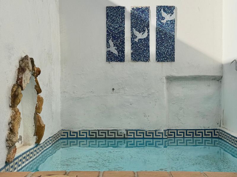 A compact outdoor pool area featuring decorative mosaic wall art, a stone feature wall, and classic Greek key tile detailing.