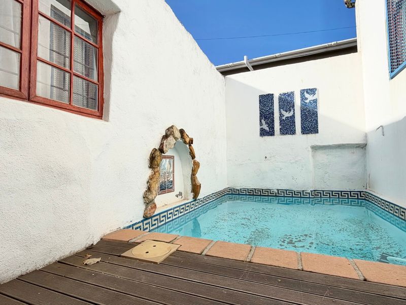 A compact outdoor pool area featuring timber decking, decorative mosaic wall art, and a built-in stone-framed wall niche.