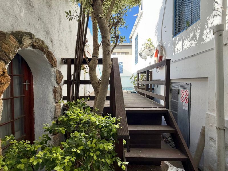A narrow exterior passage featuring a wooden staircase, timber decking, and a decorative stone archway leading to a guest house entrance.