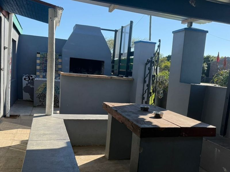 A covered outdoor patio area featuring a built-in braai, mosaic detailing, and integrated concrete seating, ideal for outdoor entertainment.