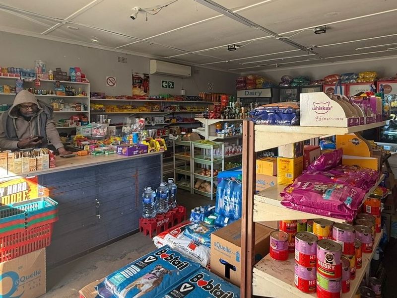 Interior view of a retail business space featuring a service counter, fixed shelving units, and wall-mounted air conditioning.