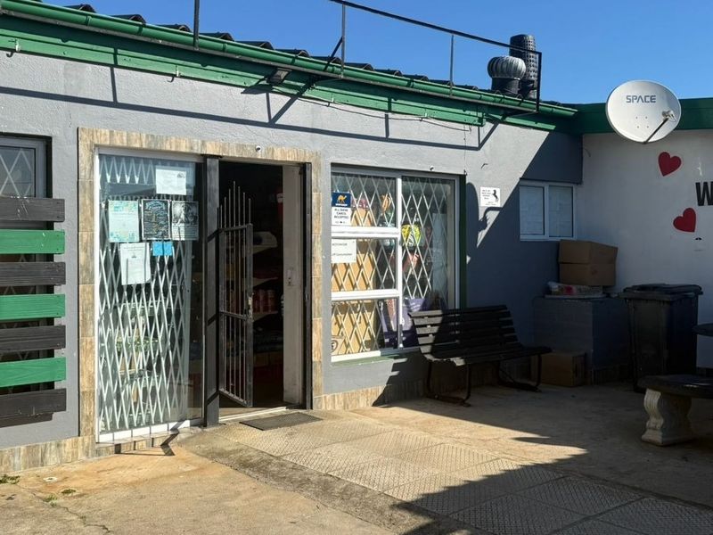 Front exterior view of a commercial property featuring a paved entrance area, security gates, and signage.