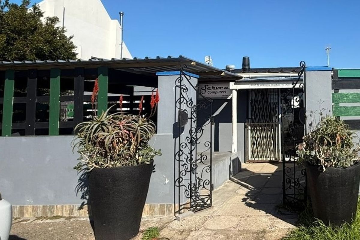 Front entrance of a commercial property featuring a paved walkway, security gate, and corrugated metal roofing.